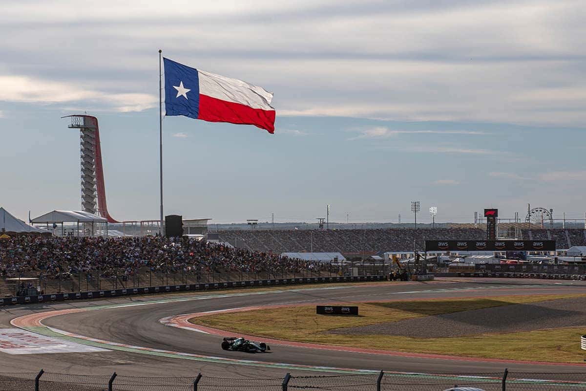 An F1 car rounds the esses at Circuit of the Americas, with the observation tower and a giant Texas flag overhead