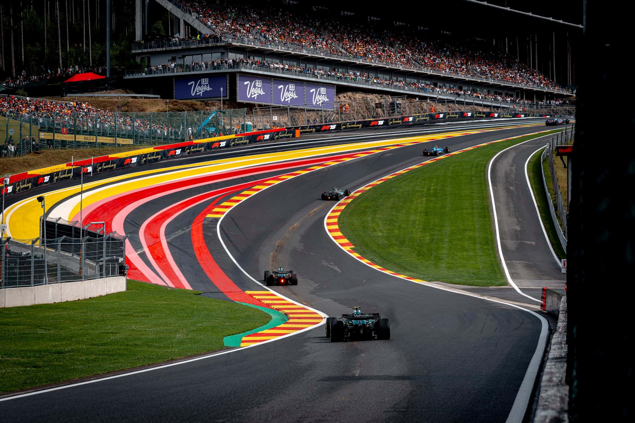 F1 cars climb through Eau Rouge and Raidillon at Spa-Francorchamps beneath grandstands full of fans