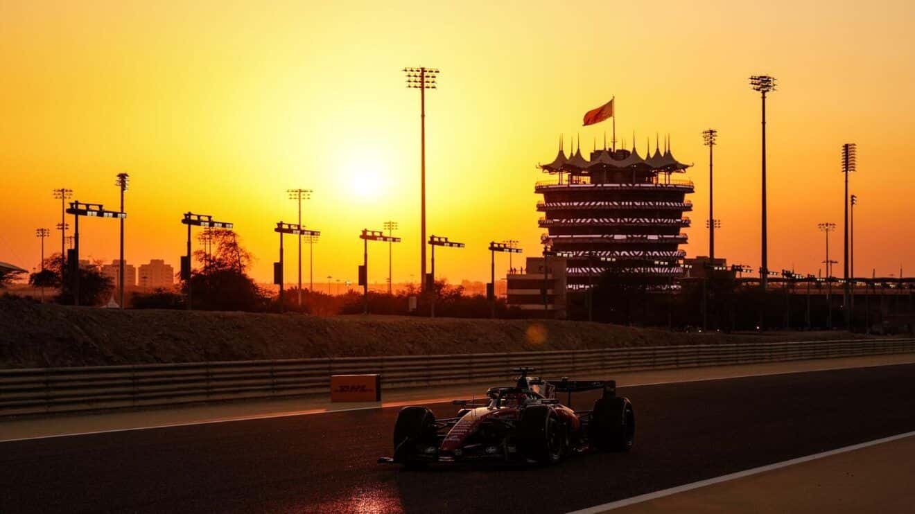 An F1 car on track at sunset at Bahrain International Circuit, with the illuminated Sakhir Tower behind
