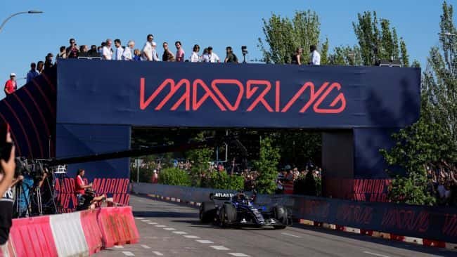 An F1 car passes beneath the Madring gateway in Madrid, with spectators watching from above