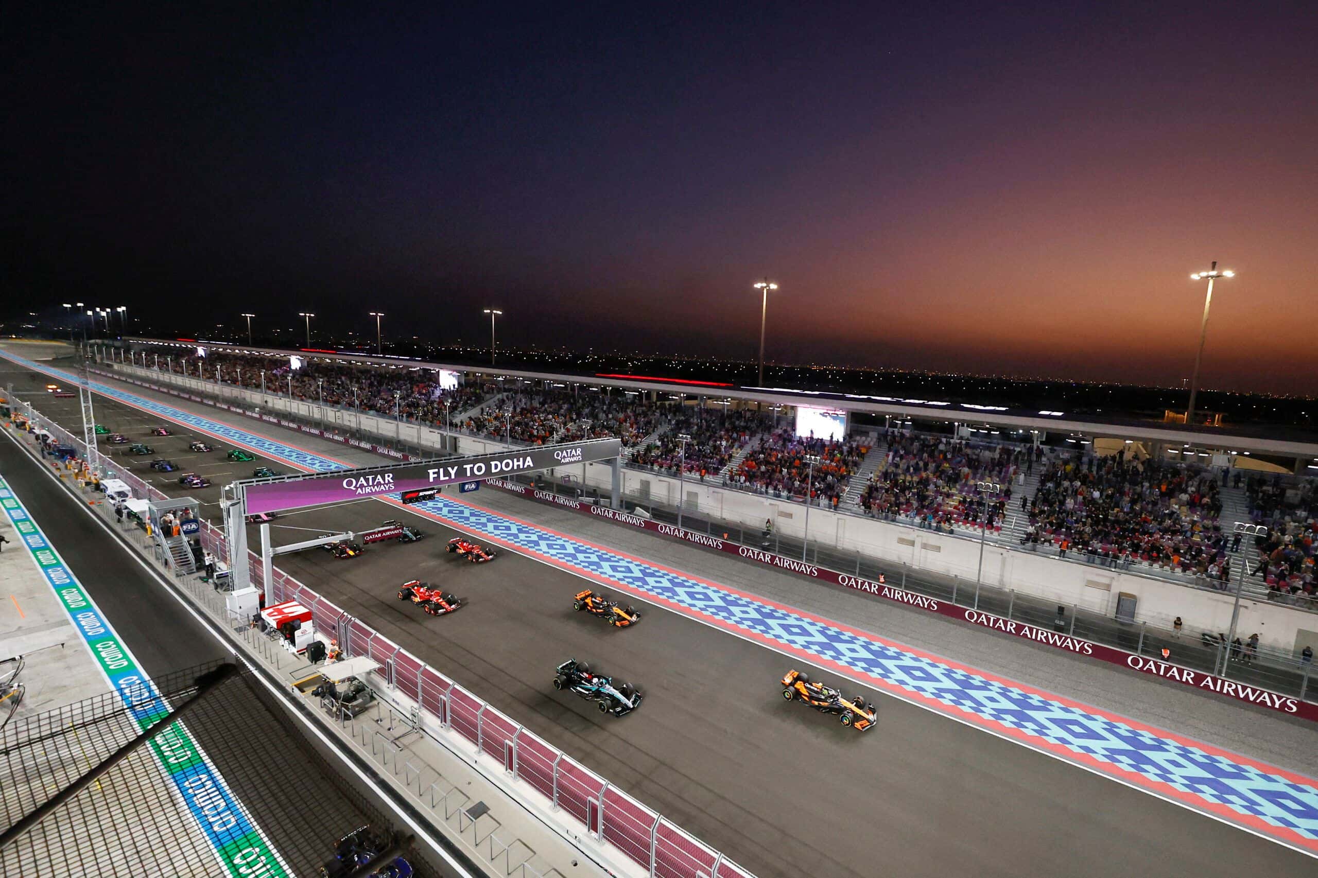 The start of a floodlit night race at Lusail International Circuit, with cars streaming past the main grandstand