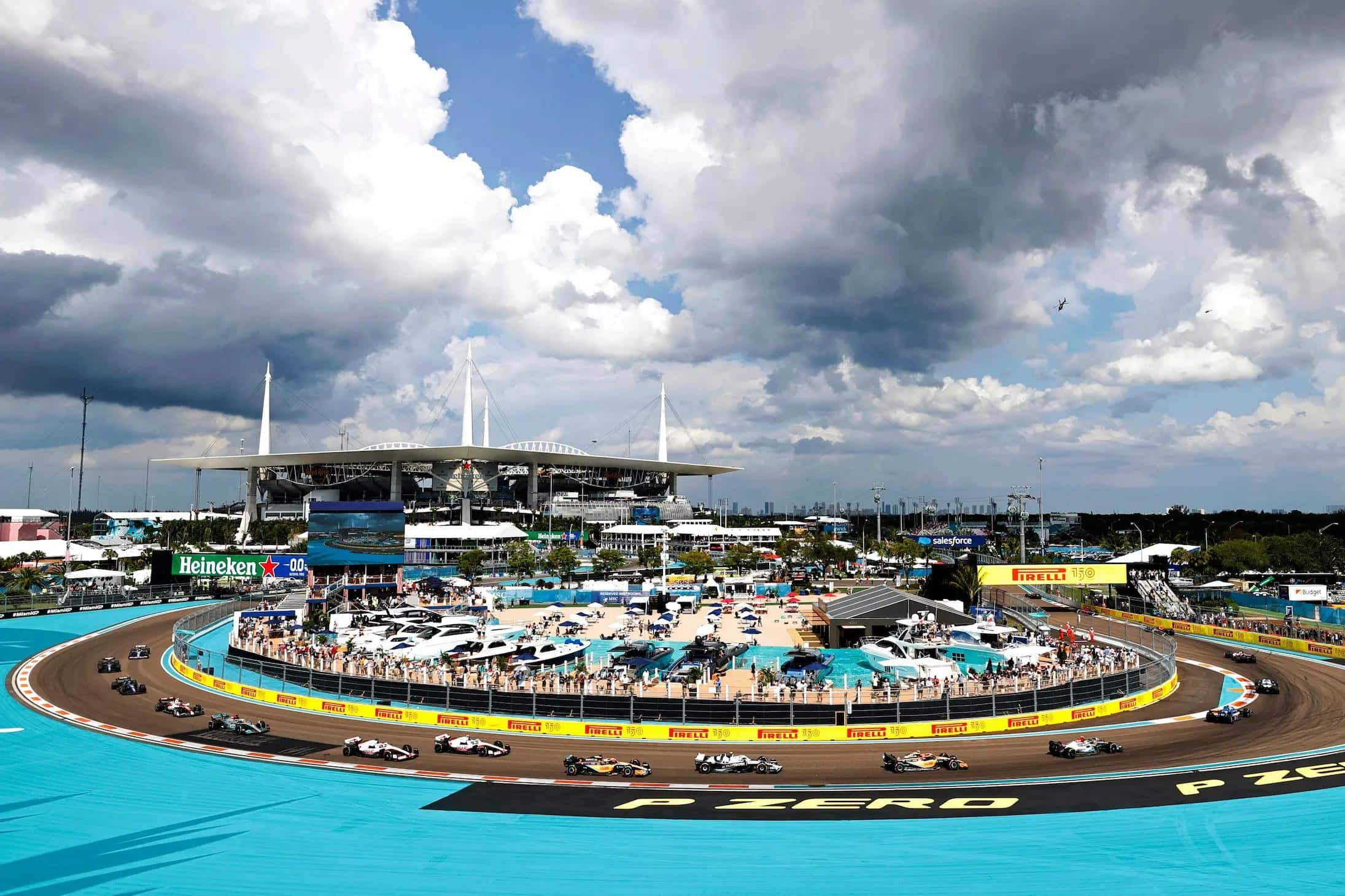 The field rounds the turquoise-lined turns at Miami International Autodrome, with Hard Rock Stadium and the marina section behind