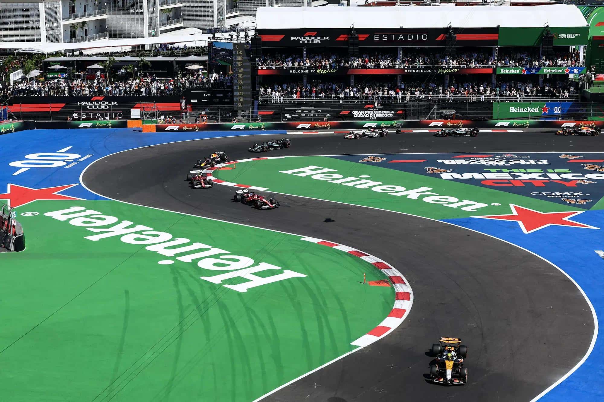 F1 cars snake through the Foro Sol stadium section at Autodromo Hermanos Rodriguez in front of packed terraces
